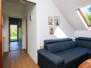 A modern living room with a dark blue sofa, a wooden floor, a white wall with framed pictures, and a skylight. - 6 Person Holiday Home in Toftlund (Toftlund)
