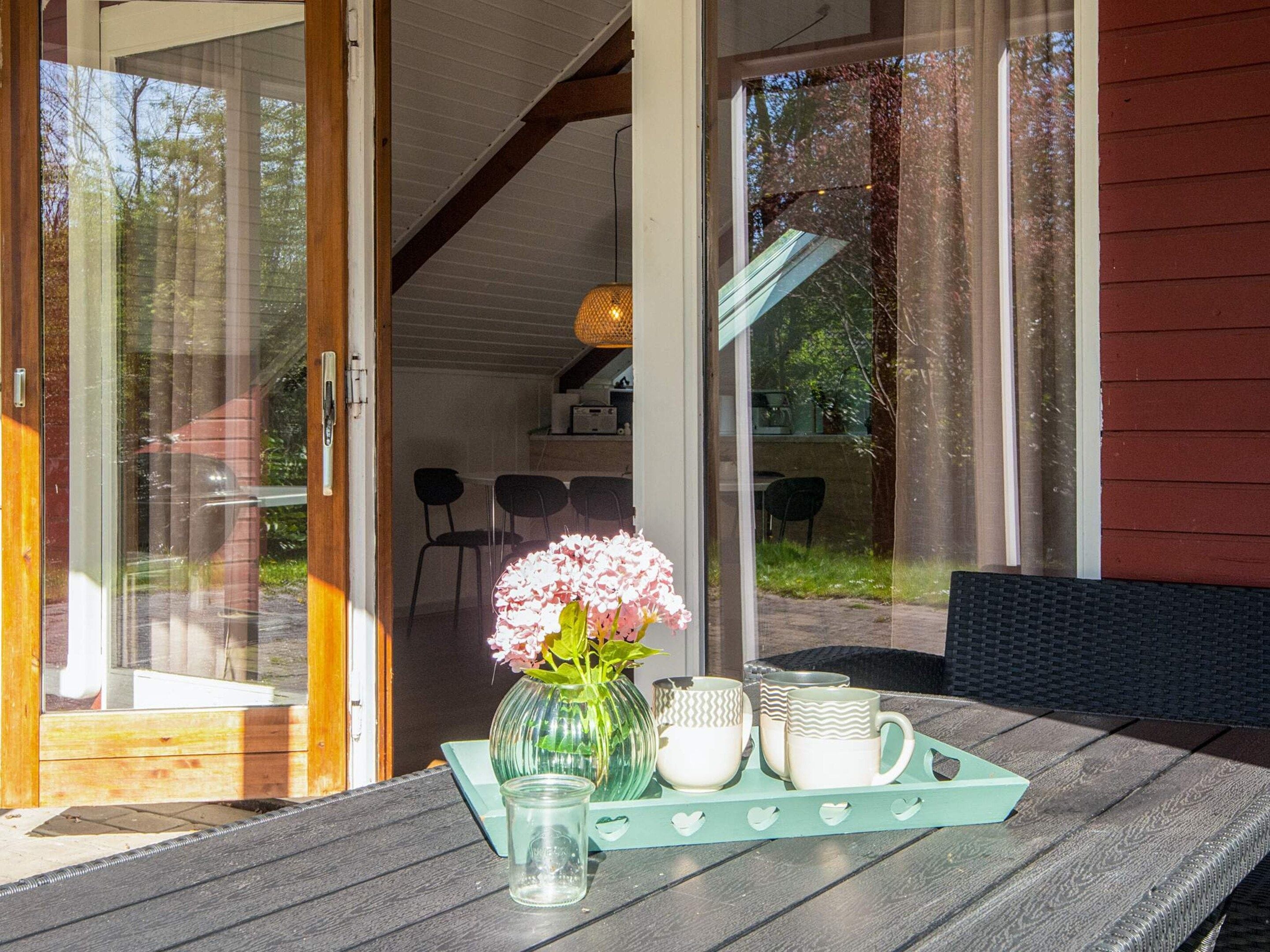 An open door leading to a room with a table set with a vase of flowers, a glass, and a tray with cups.