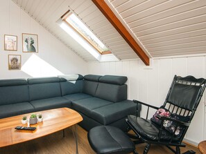 Una habitación acogedora con un sofá seccional, una mesa de centro de madera, un sillón de cuero negro y un tragaluz.