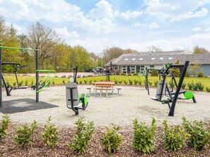 Un área de gimnasio al aire libre con equipo de ejercicio, una mesa de picnic y un edificio al fondo.
