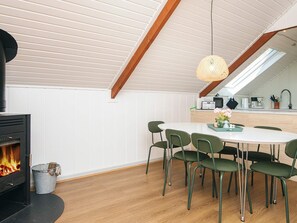 A modern kitchen with a wood-burning stove, a dining table with chairs, and a hanging light fixture.