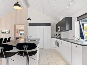 Una cocina moderna con armarios blancos, electrodomésticos de acero inoxidable y un comedor con sillas negras.