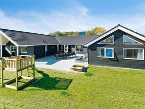Une maison moderne à deux étages dotée d’un patio, d’une terrasse en bois et d’un espace de jeux.