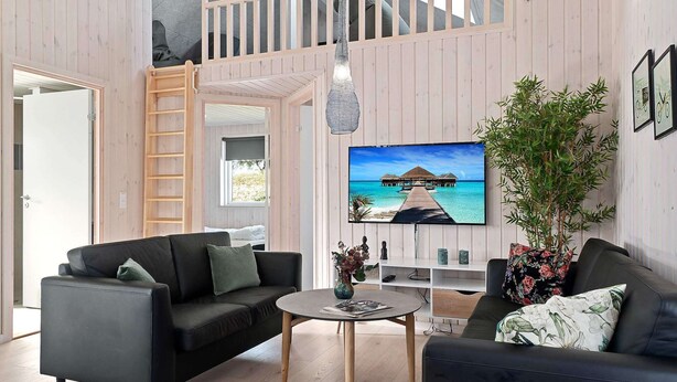 A modern living room with a black sofa, a round coffee table, and a TV mounted on the wall. - Holiday Home in Kappeln (Kappeln)