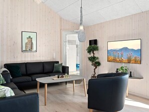 A modern living room with a black sofa, a coffee table, and a TV mounted on the wall. - Holiday Home in Kappeln (Kappeln)