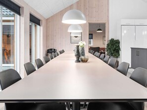 A conference room with a long table, black chairs, white pendant lights, and a potted plant.