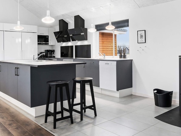 A modern kitchen with a large island, bar stools, and a view of the outside. - Holiday Home in Kappeln (Kappeln)