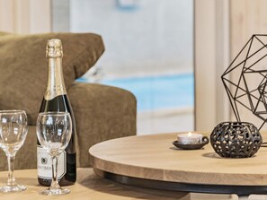 En flaska champagne, två vinglas, en dekorativ metallkula och ett träbord i ett rum med utsikt över en pool.