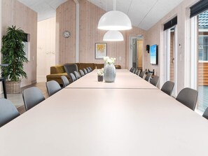 A conference room with a long table, chairs, a potted plant, a clock, and a large window.