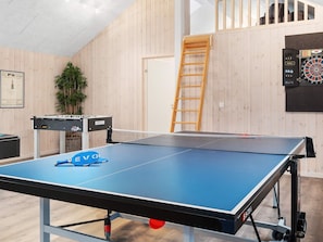 A ping pong table with a blue table and net, a foosball table, a dartboard, and a ladder against a wooden wall. - Holiday Home in Kappeln (Kappeln)