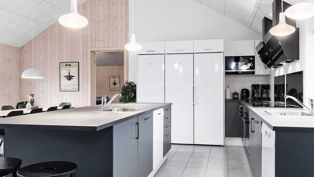 Una cucina moderna con isola centrale, elettrodomestici bianchi e illuminazione a sospensione.