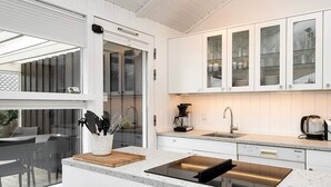 Una cocina moderna con armarios blancos, horno integrado, lavamanos y cafetera.