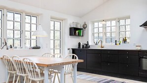 Eine moderne Küche mit Holzesstisch und Stühlen, großen Fenstern und einer schwarzen Arbeitsplatte.
