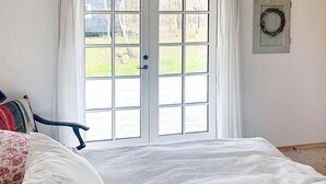 Ein Schlafzimmer mit Bett, Stuhl, Fenster mit Blick auf einen Garten und einem Kranz an der Wand.