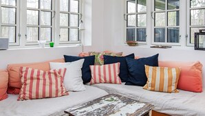 Ein gemütliches Zimmer mit großem Fenster, einer Couch mit gestreiften Kissen und einem rustikalen Holztisch.