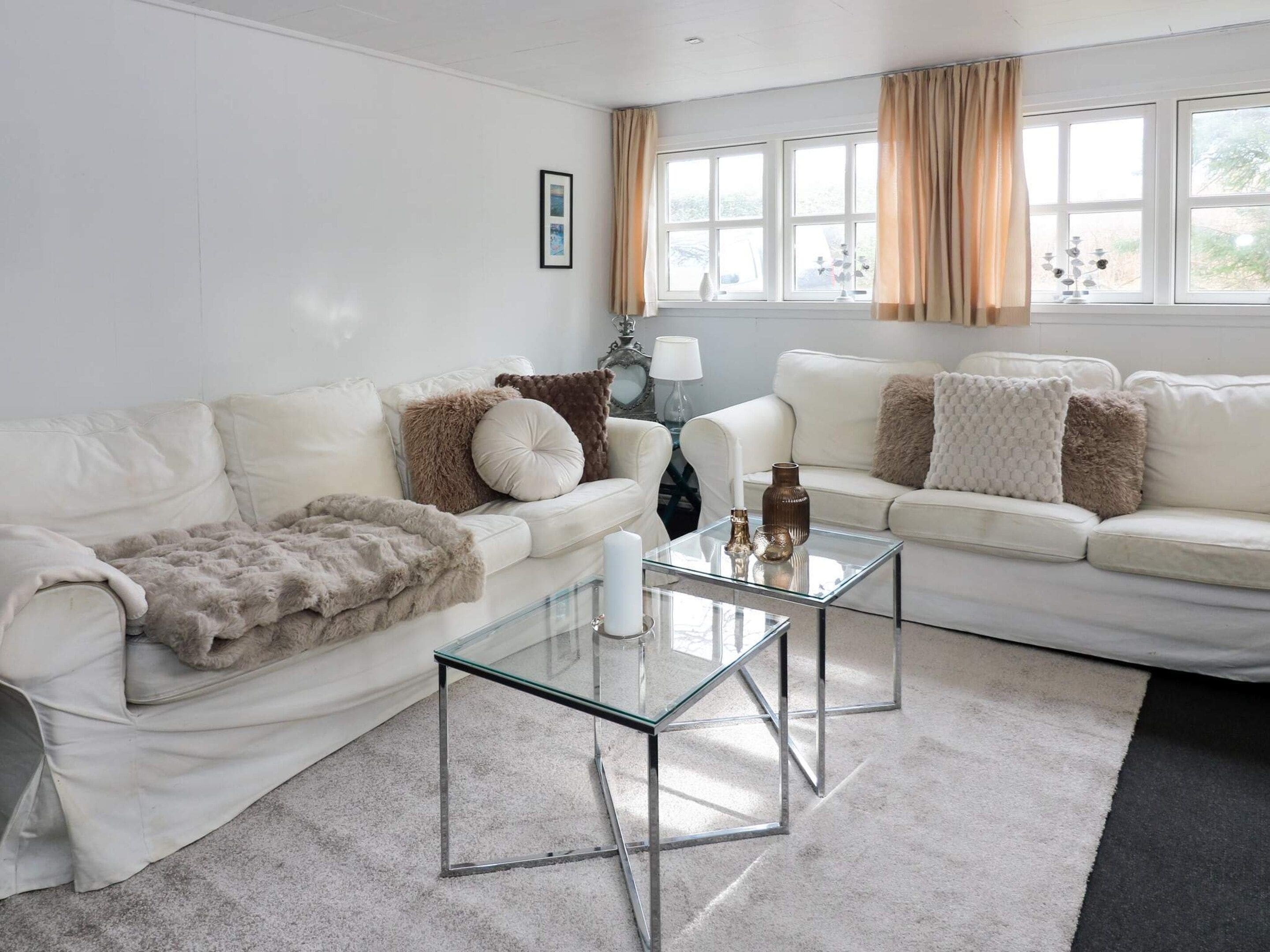 Una sala de estar moderna con dos sofás blancos, una mesa de centro de vidrio y un ventanal con cortinas.