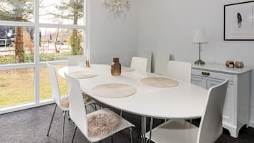 Un comedor con mesa blanca, sillas y una araña.