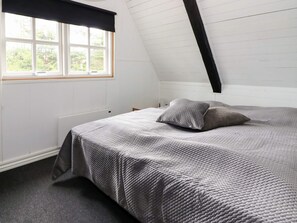 A bedroom with a sloped ceiling, a large window with a black valance, a bed with a grey quilt, and a radiator. - 4 Person Holiday Home in Hadsund (Hadsund)