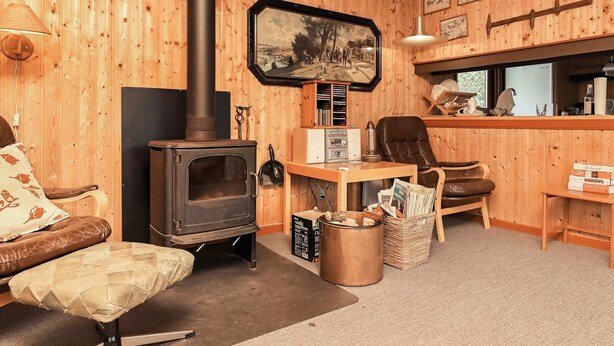 A cozy room with a wood-burning stove, a leather chair, a wooden desk, and a bookshelf. - Rustic Retreat in Klitmoller-by Traum (Thisted)