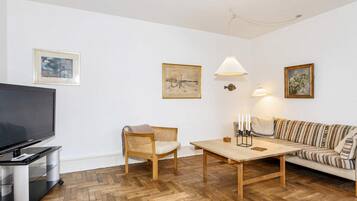 Una sala de estar con televisión, sofá, mesa y sillón.