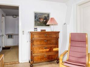 A wooden dresser with drawers, a pink lamp, and a framed painting on the wall.