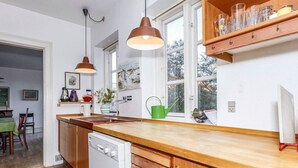 A kitchen with wooden cabinets, a dishwasher, a window with a view, and a shelf with glasses. - 5 Person Holiday Home in Logstor (Logstor)