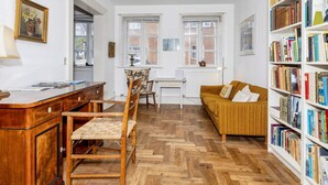 A room with a wooden herringbone floor, a wooden desk with a chair, a sofa, and a bookshelf filled with books. - 5 Person Holiday Home in Logstor (Logstor)