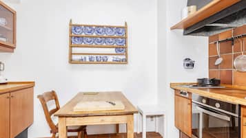 Una cocina con una mesa de madera, sillas, un colgador para ollas y una estufa.