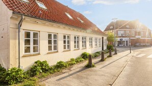 A building with a red-tiled roof, multiple windows, and a sidewalk with greenery and bollards. - 5 Person Holiday Home in Logstor (Logstor)