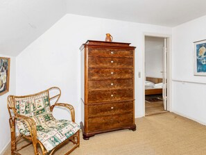 A room with a wooden dresser, a wicker chair with a patterned cushion, and a bed in the background. - 5 Person Holiday Home in Logstor (Logstor)