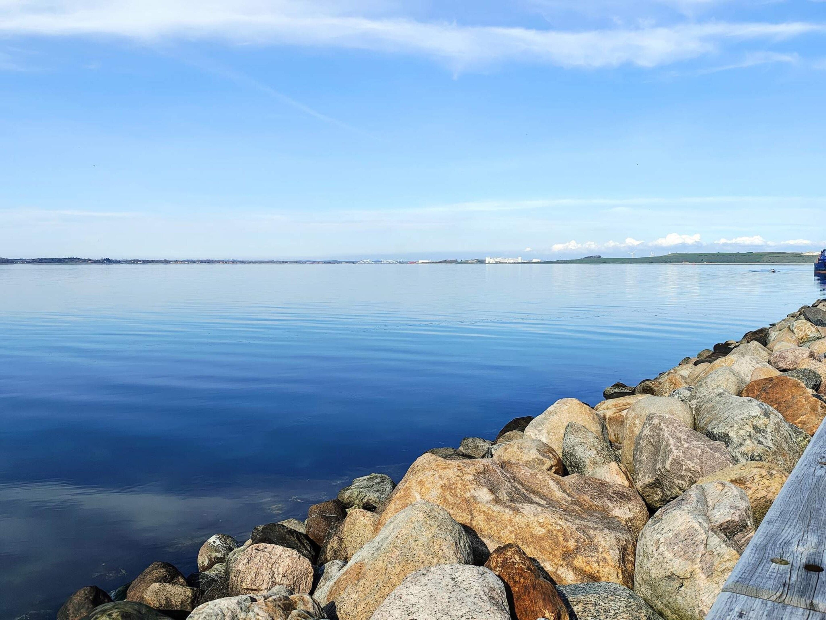A calm body of water with a rocky shoreline and distant buildings.