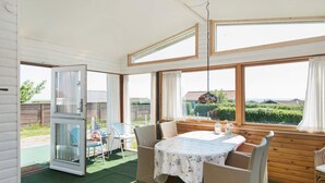 A cozy room with a table and chairs, large windows, and a view of greenery outside.