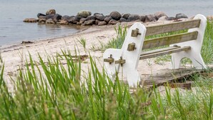 A bench by a lake with a rocky shoreline and greenery in the foreground.