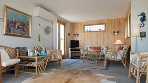 A cozy living room with wooden walls, a large rug, wicker furniture, and a painting on the wall.