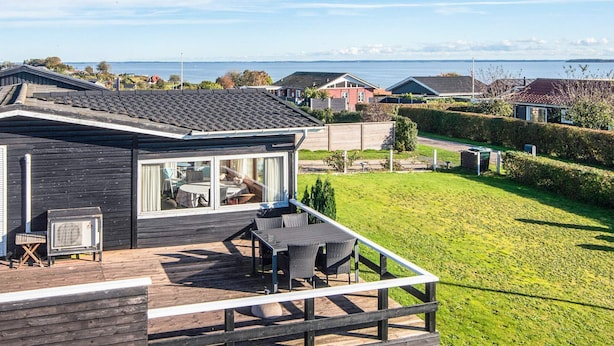 A modern house with a deck, large windows, and a view of the sea.