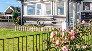 A modern mobile home with large windows, a fenced yard, and blooming roses.