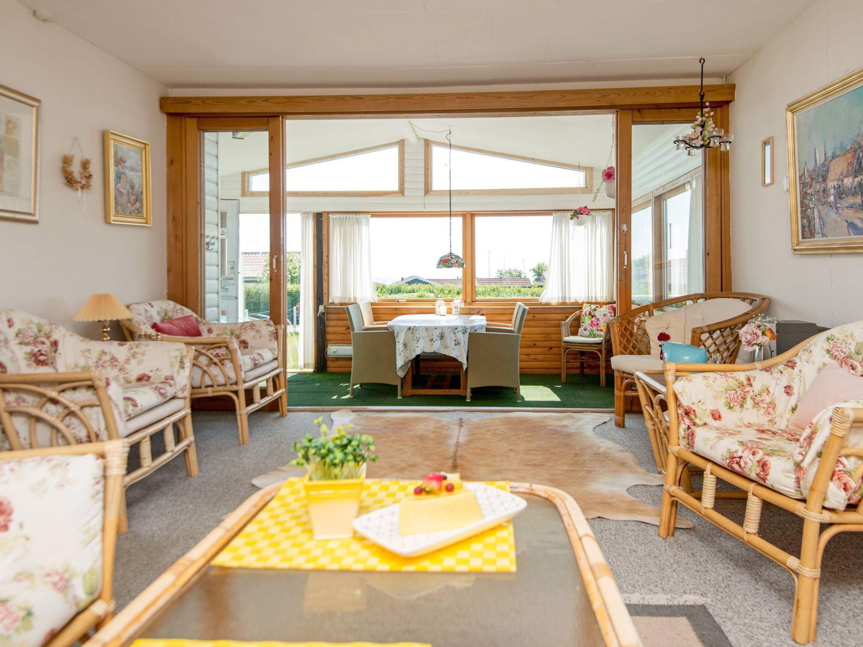 A cozy room with wicker furniture, a dining table, and a view through large windows.