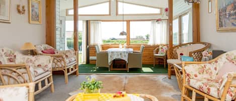 A cozy room with wicker furniture, a dining table, and a view through large windows.