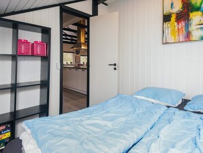 A bedroom with a bed, a shelf with pink baskets, and a door leading to a kitchen. - 6 Person Holiday Home in Toftlund (Toftlund)