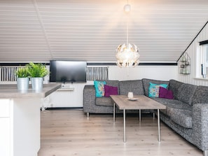 Uma sala de estar moderna com um sofá cinzento, uma mesa de centro de madeira, uma televisão de tela plana e um candelabro singular.