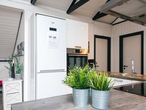 A modern kitchen with a built-in refrigerator, a microwave, and a stove. There are two potted plants on the counter.