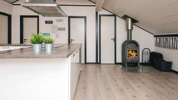 A modern kitchen with a central island, a wood-burning stove, and a dining area with a chair and a trash bin.