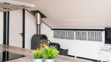 A modern kitchen with a built-in wood stove, a dining area with a wooden table, and a TV mounted on the wall.