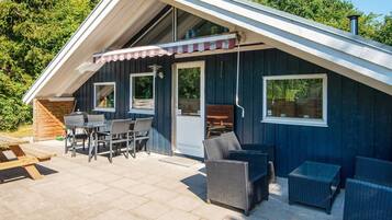 A cozy, dark wooden cabin with a sloped roof, outdoor seating area, and large windows.