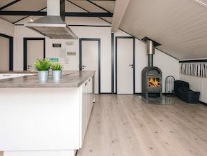 A modern kitchen with a central island, a wood-burning stove, and a dining area with a chair and a trash bin. - 6 Person Holiday Home in Toftlund (Toftlund)