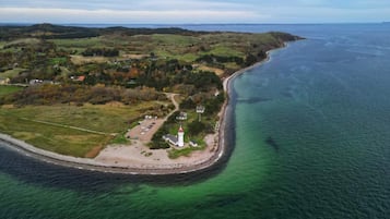 An aerial view of a coastal area with a lighthouse, a parking lot, and a small settlement.