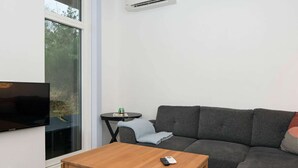 A modern living room with a grey sofa, a wooden coffee table, a TV, and a small round table with a green cup. - Holiday Home in Knebel (Knebel)