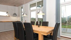 A modern kitchen with a wooden table and black chairs, large windows, and pendant lights. - Holiday Home in Knebel (Knebel)