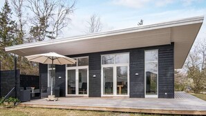 A modern house with a flat roof, large glass windows, and a wooden deck. - Holiday Home in Knebel (Knebel)