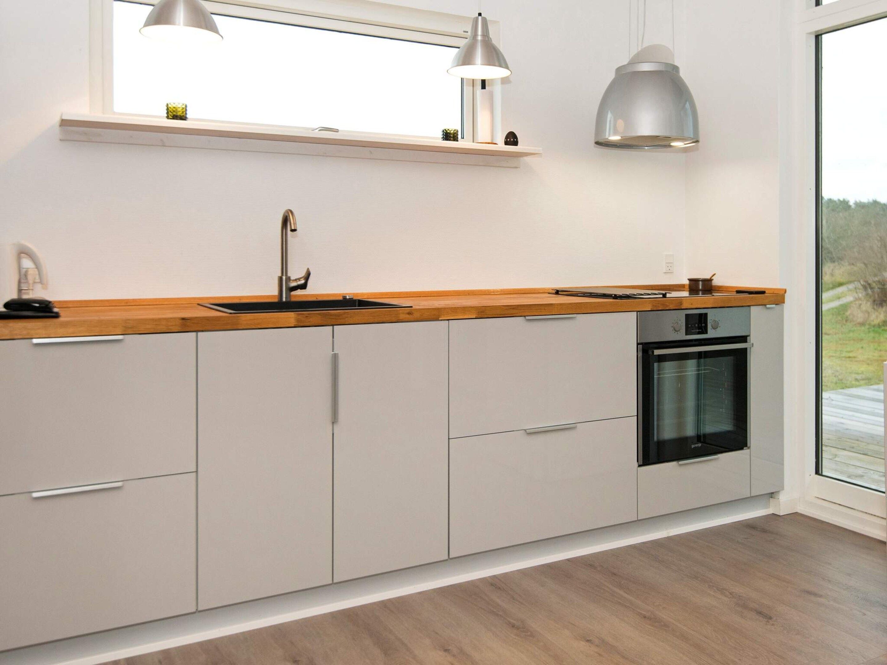 A modern kitchen with a wooden countertop, a built-in oven, and pendant lighting.